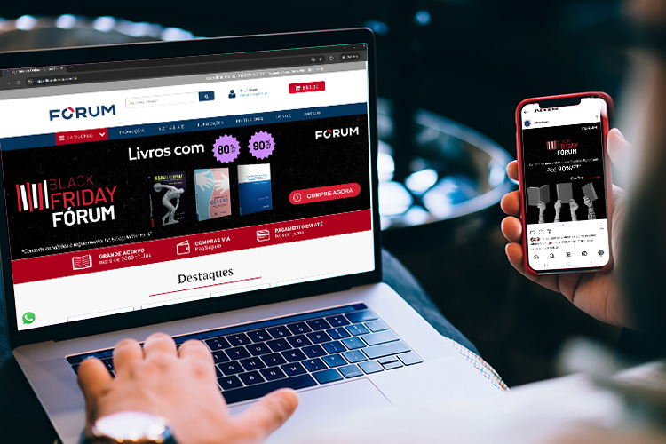 Close de um jovem segurando um celular e mexendo no computador. A tela do dispositivo mostra o site da Black Friday FÓRUM